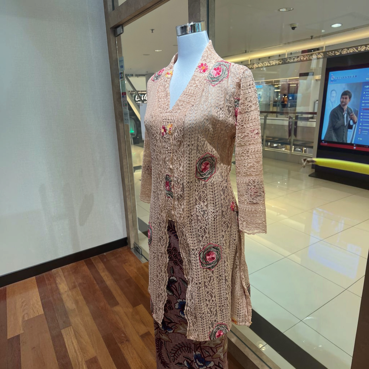 POYA brown long kebaya top in embroidered lace with floral accents on a mannequin in a retail store setting